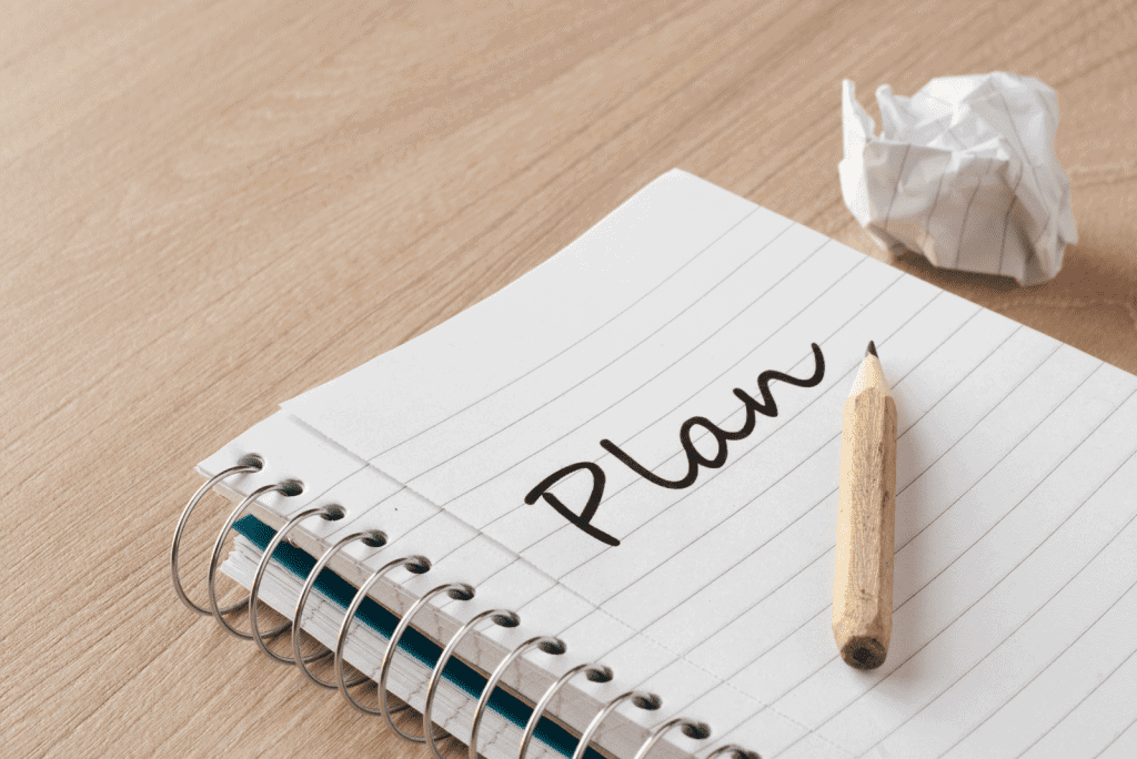 An image of a lined notepad with PLan written & a pencil resting on it