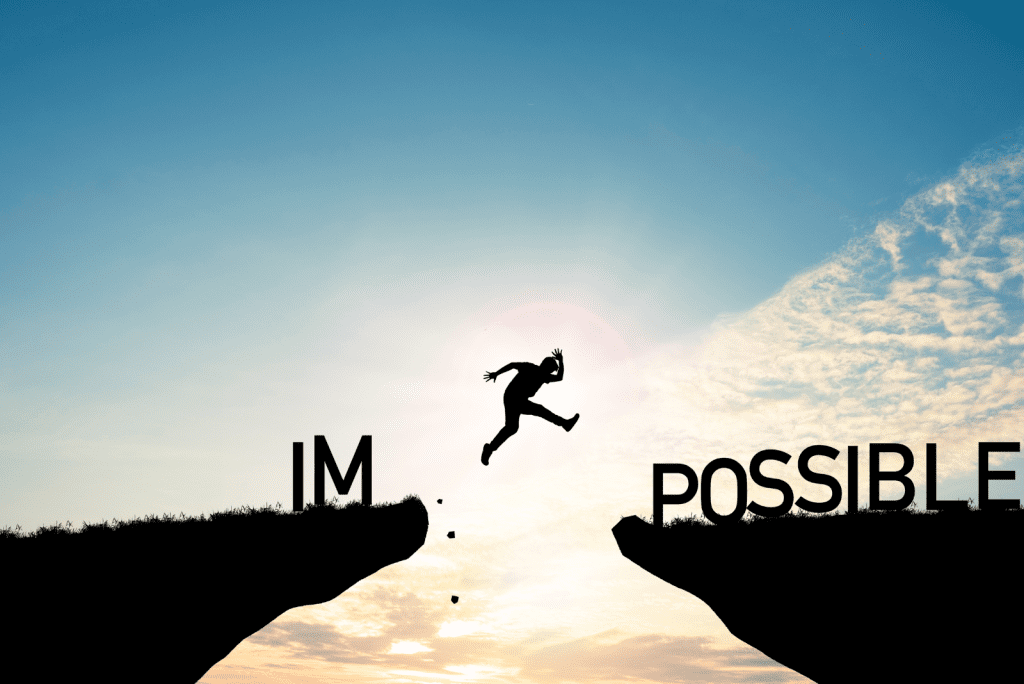 Image of a man jumping between two mountain edges. The sun behind so it's a shaow and the word impossible issplit across the edges, with "IM" staying on the left with the man jumping towards "POSSIBLE"