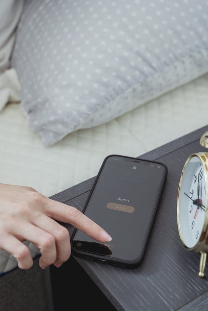 Daily Habits: From above of hand of crop anonymous female turning off alarm on mobile phone in bedroom in morning time