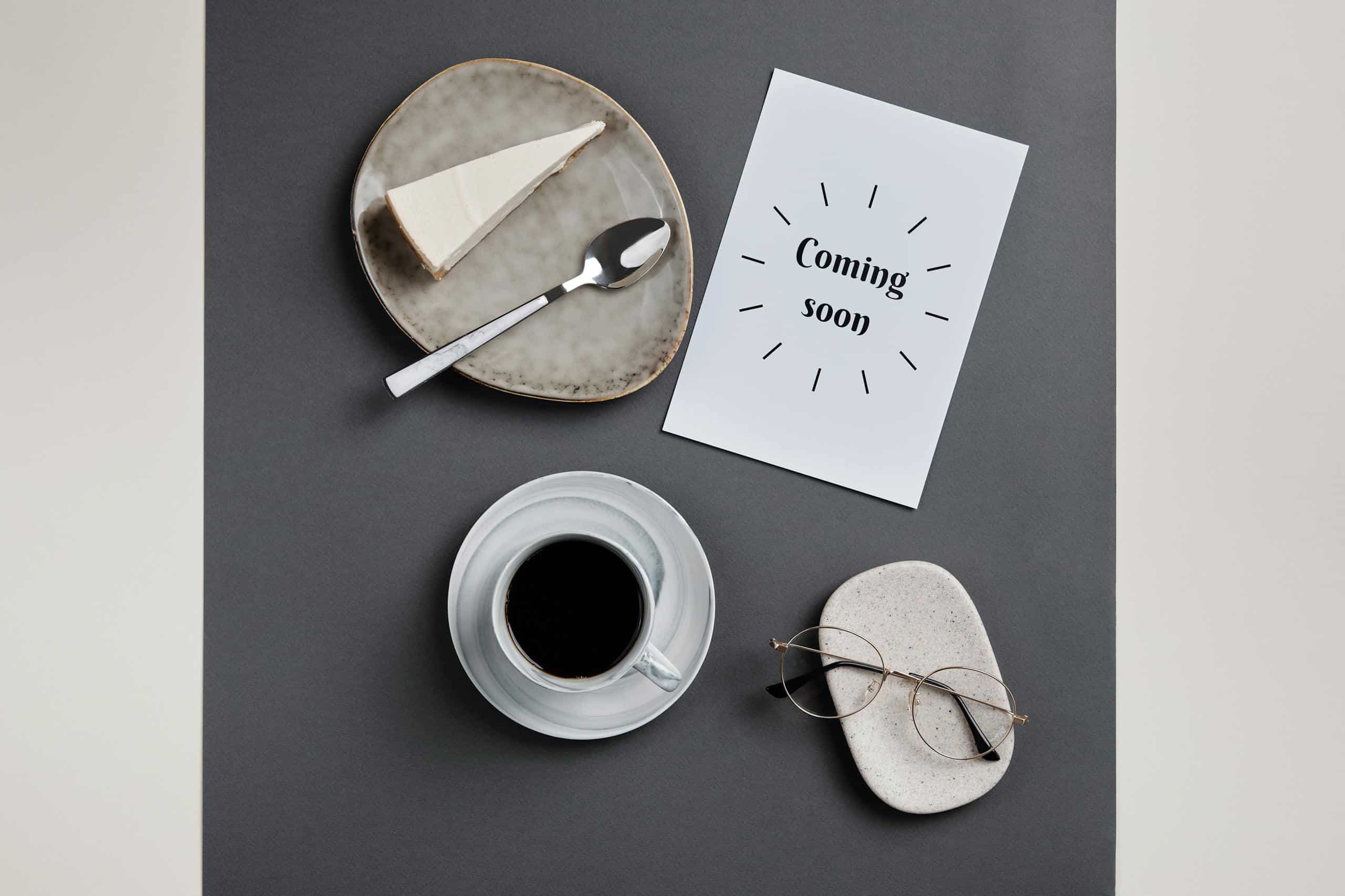 Coming Soon! A Slice of Cake and a Cup of Coffee Near the White Paper and Eyeglasses