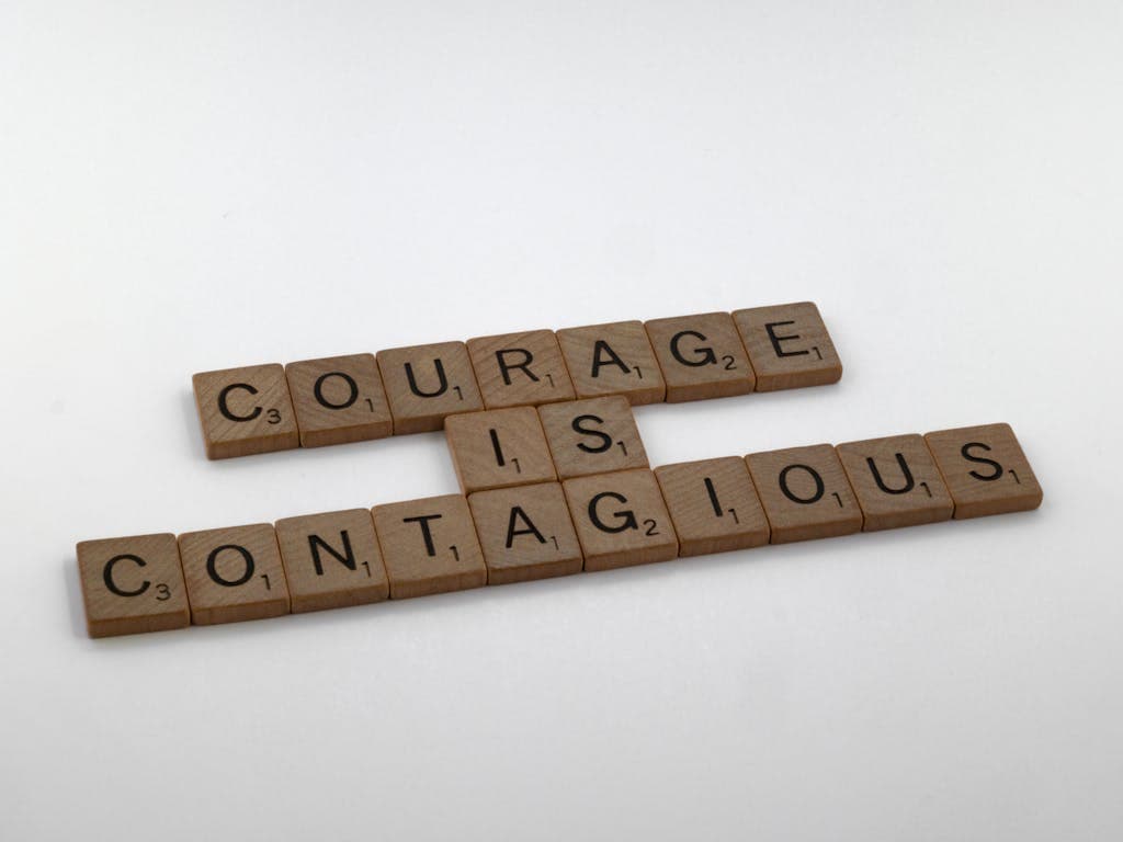 Scrabble tiles spelling out 'Courage is Contagious' on a white surface.